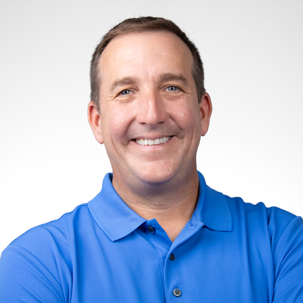 Man with short brown hair in a blue polo shirt stands smiling with arms crossed, representing digital healthcare for medbridge.