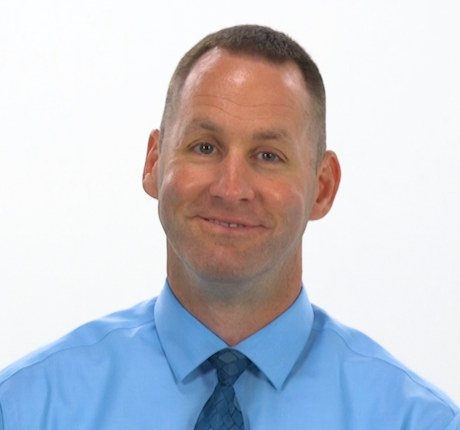 A man in a light blue shirt and blue tie smiles against a white background, representing medbridge’s digital healthcare solutions.